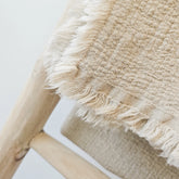Close-up of a textured beige linen blanket with fringes on a white background