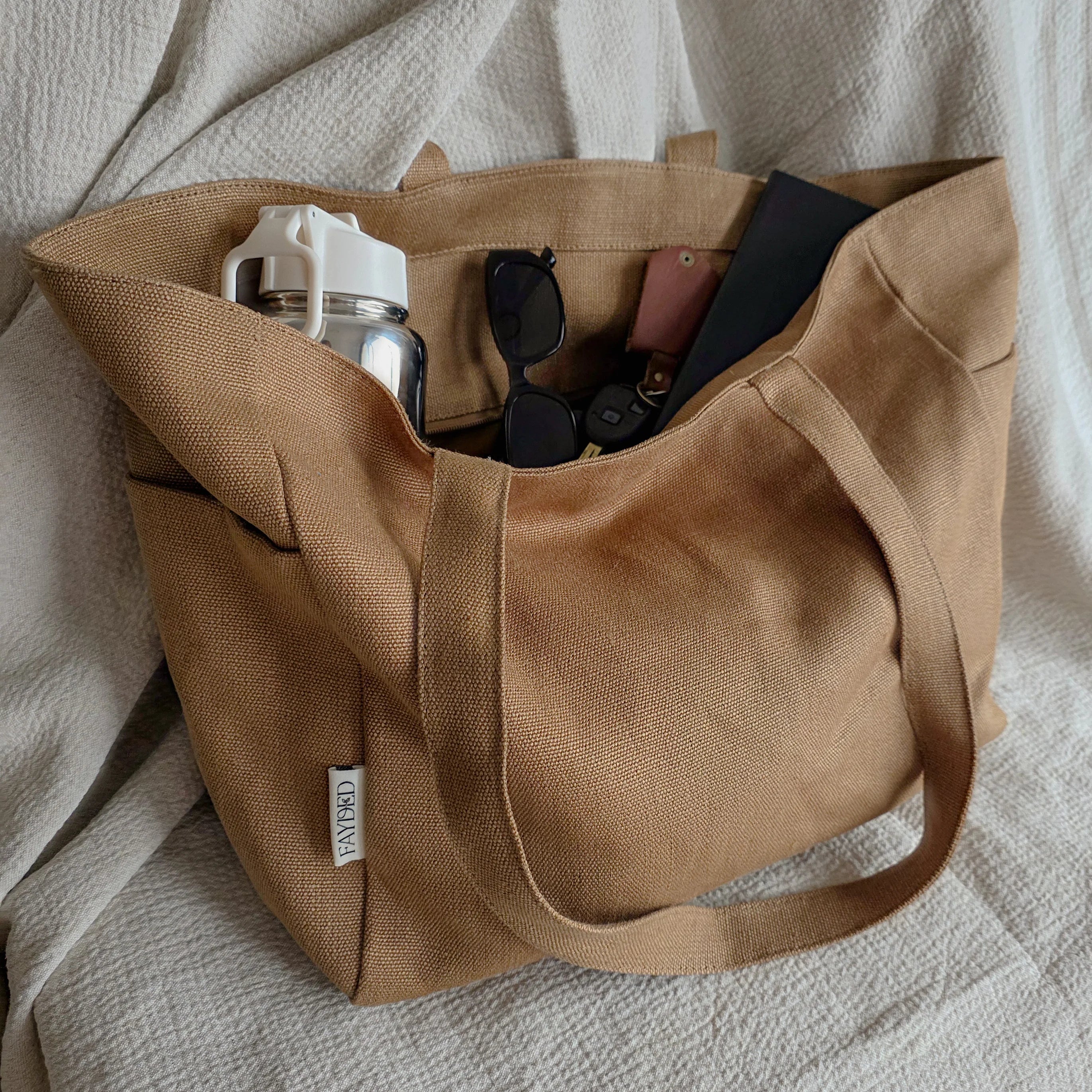 Brown tote bag with sunglasses and a phone on a textured surface