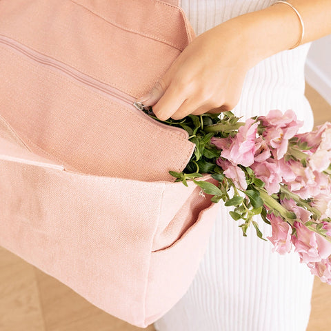 Person holding a bouquet of pink flowers in a pink linen tote bag with zipper