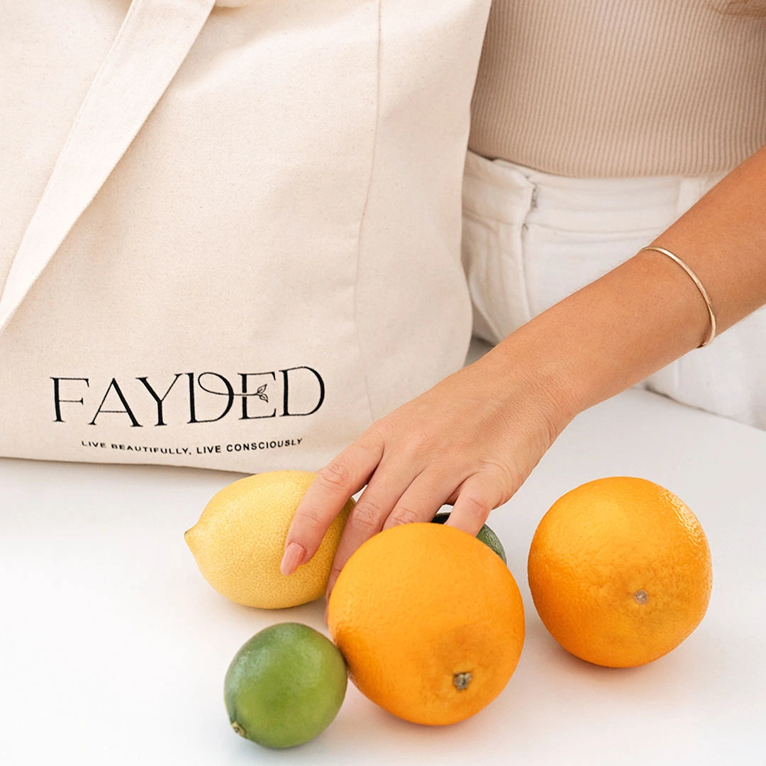 Person holding oranges with a 'FAYDED' reusable cotton bag in the background