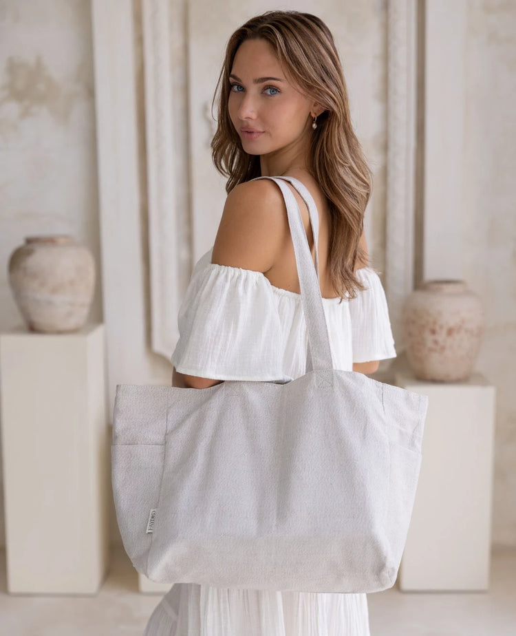 Woman holding a light gray 100% linen tote bag in a neutral setting. 