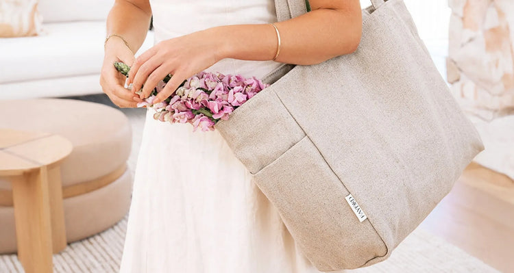 Person holding an oatmeal natural flax linen handbag with flowers, sitting on a couch.