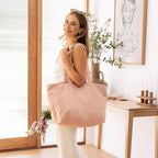Woman holding a pink flax tote bag in a bright room with a vase and plant.