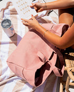 Person holding a pink tote with a towel and tumbler nearby a pool setting