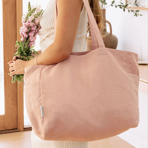 Person holding a pink tote bag and flowers indoors