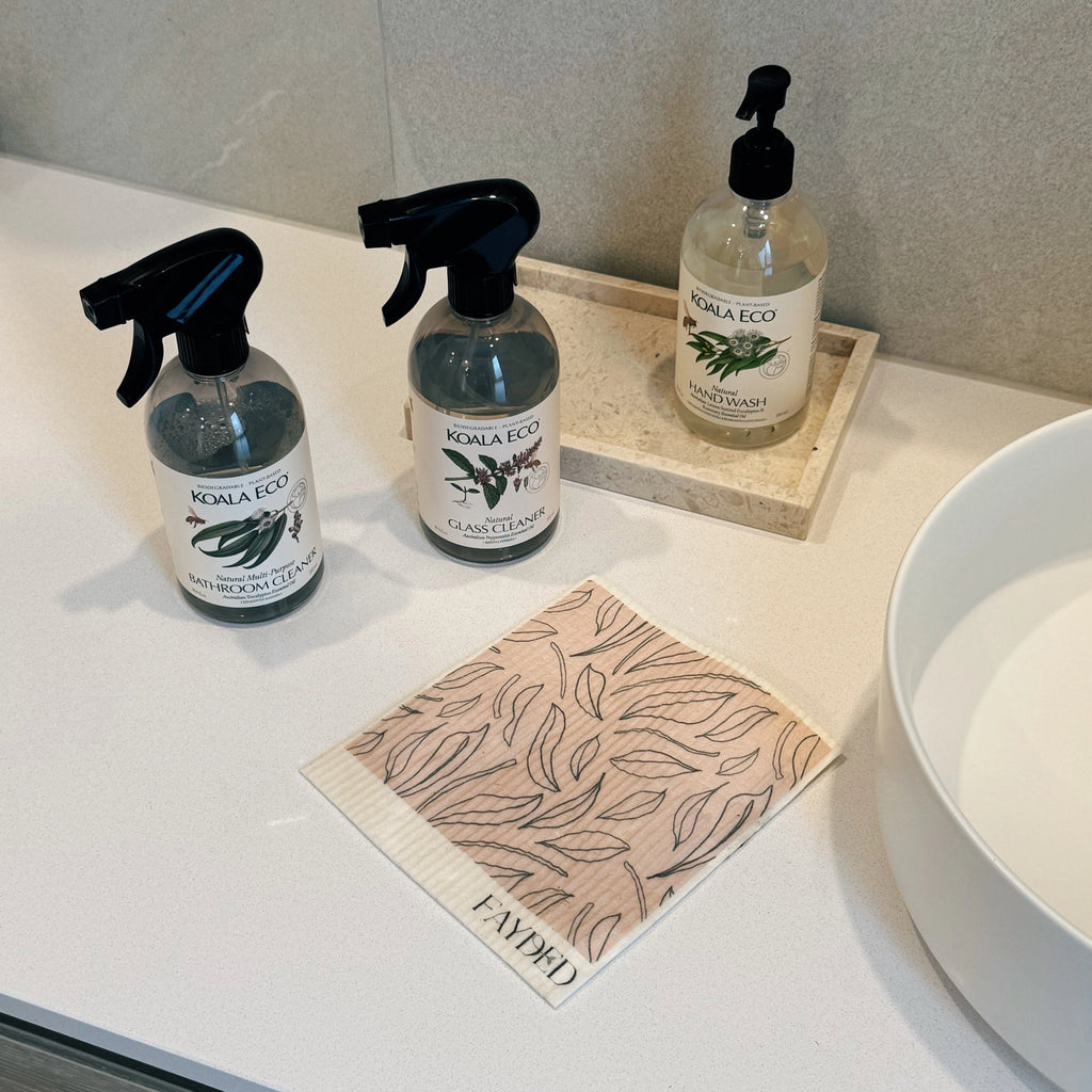Three bottles of Koala Eco cleaning products on a bathroom counter with a cloth.