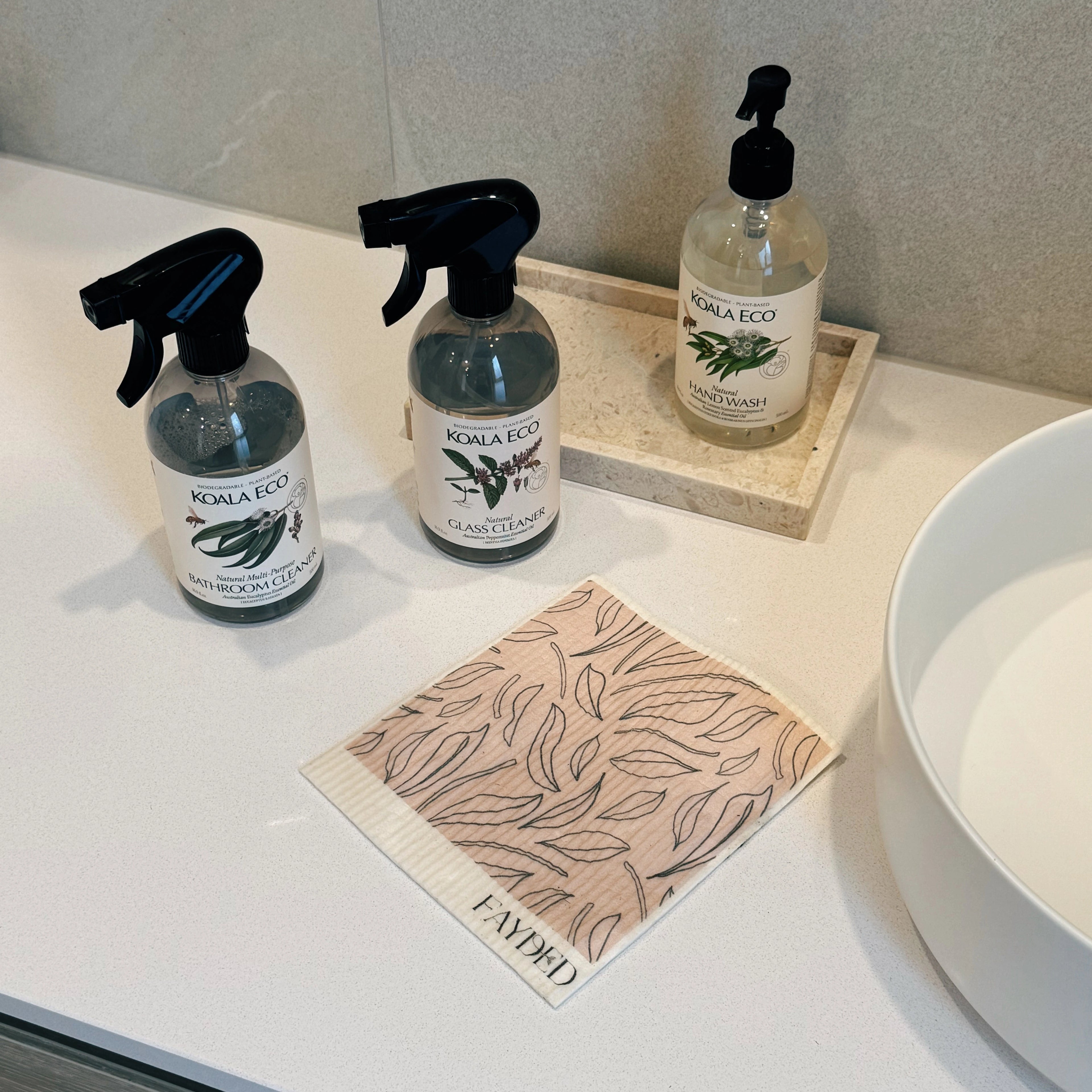 Three bottles of Koala Eco cleaning products on a bathroom counter with a cloth.