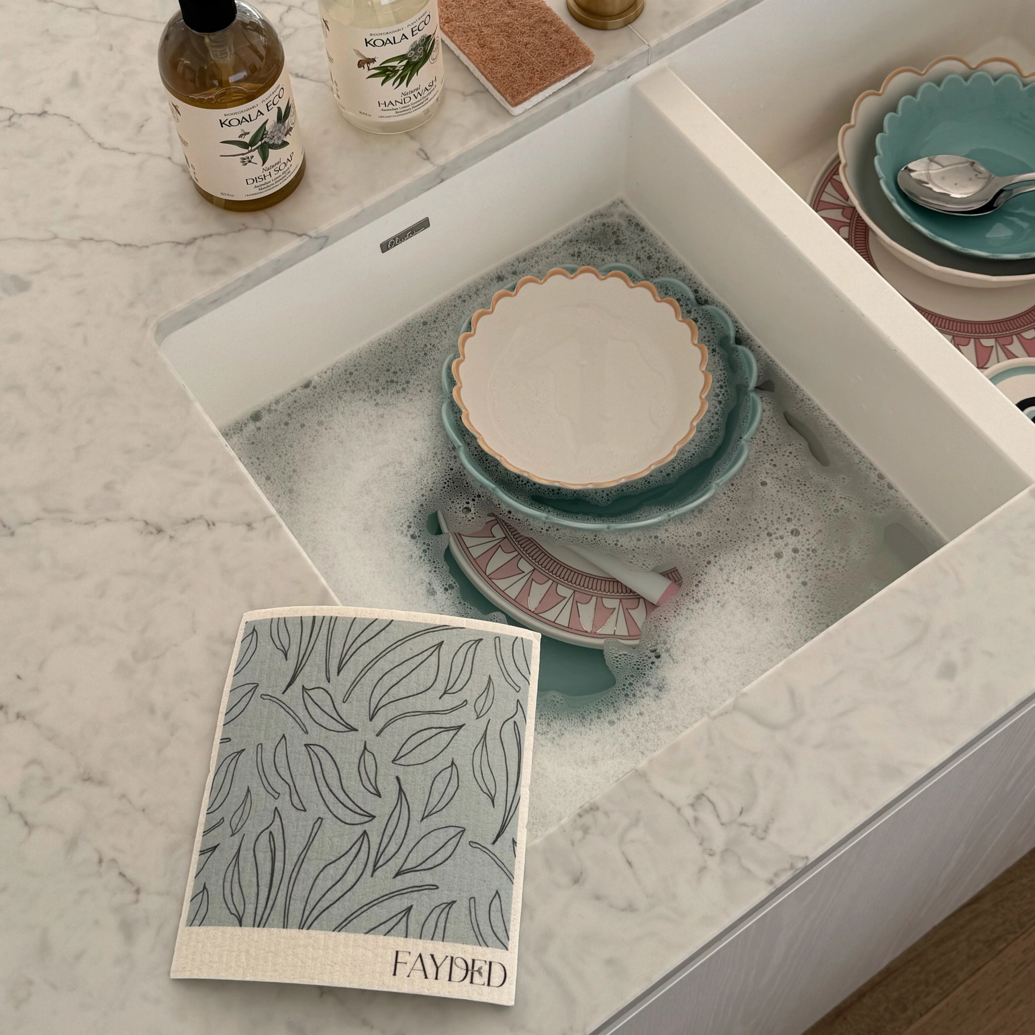 Dishwasher with soapy water and ceramic dishes, with a 'FAYDED' product card on a marble countertop. Main image