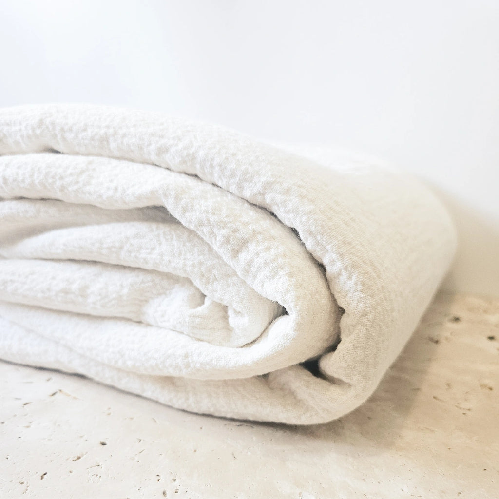 Folded white linen and cotton blanket on a light marble surface