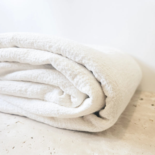 Folded white linen and cotton blanket on a light marble surface