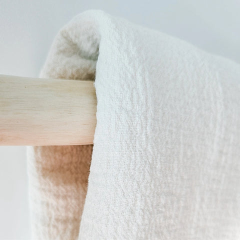 White linen blanket draped over a wooden rod on a light gray background